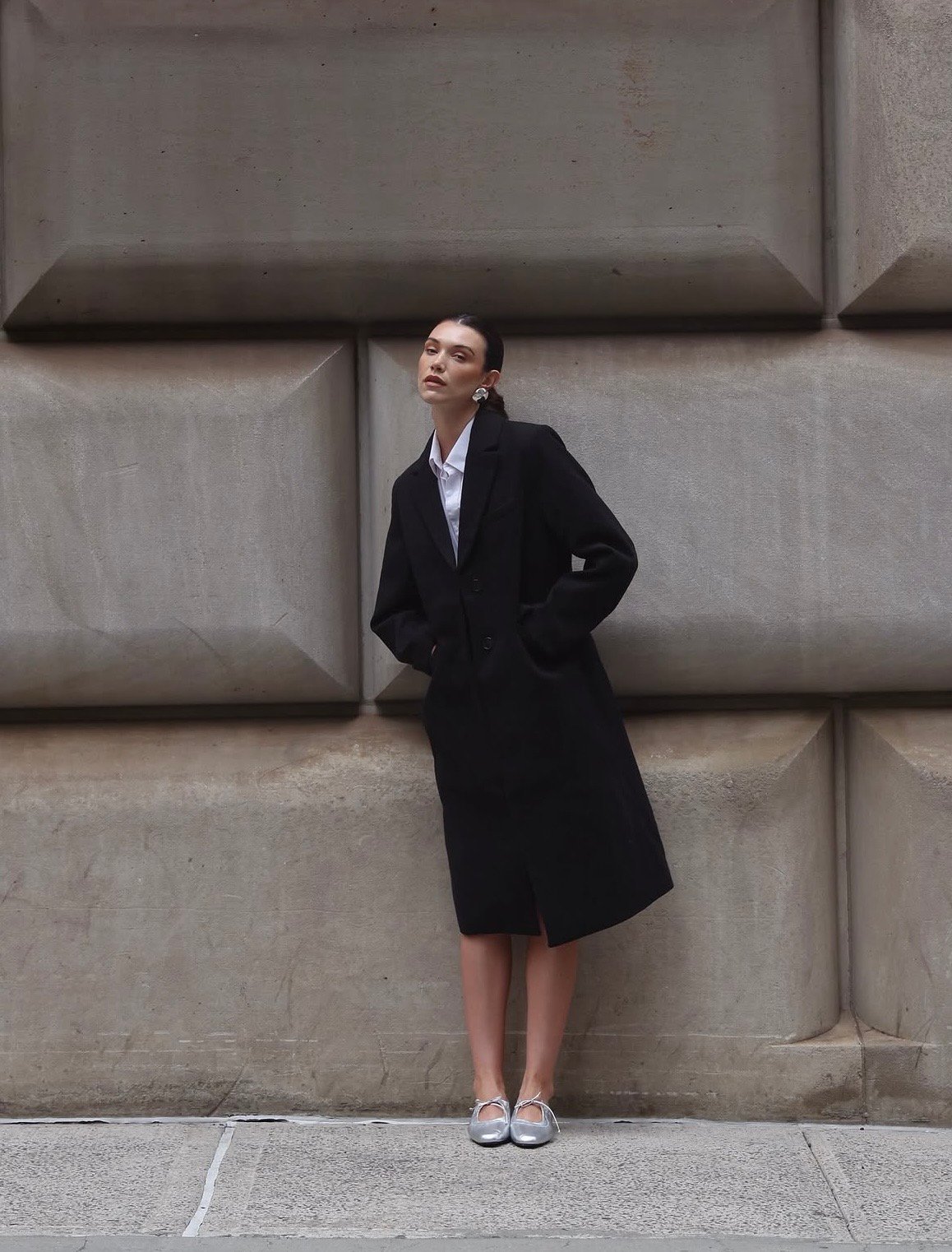 ALTA Shoes: modelo con abrigo negro frente a una fachada arquitectónica