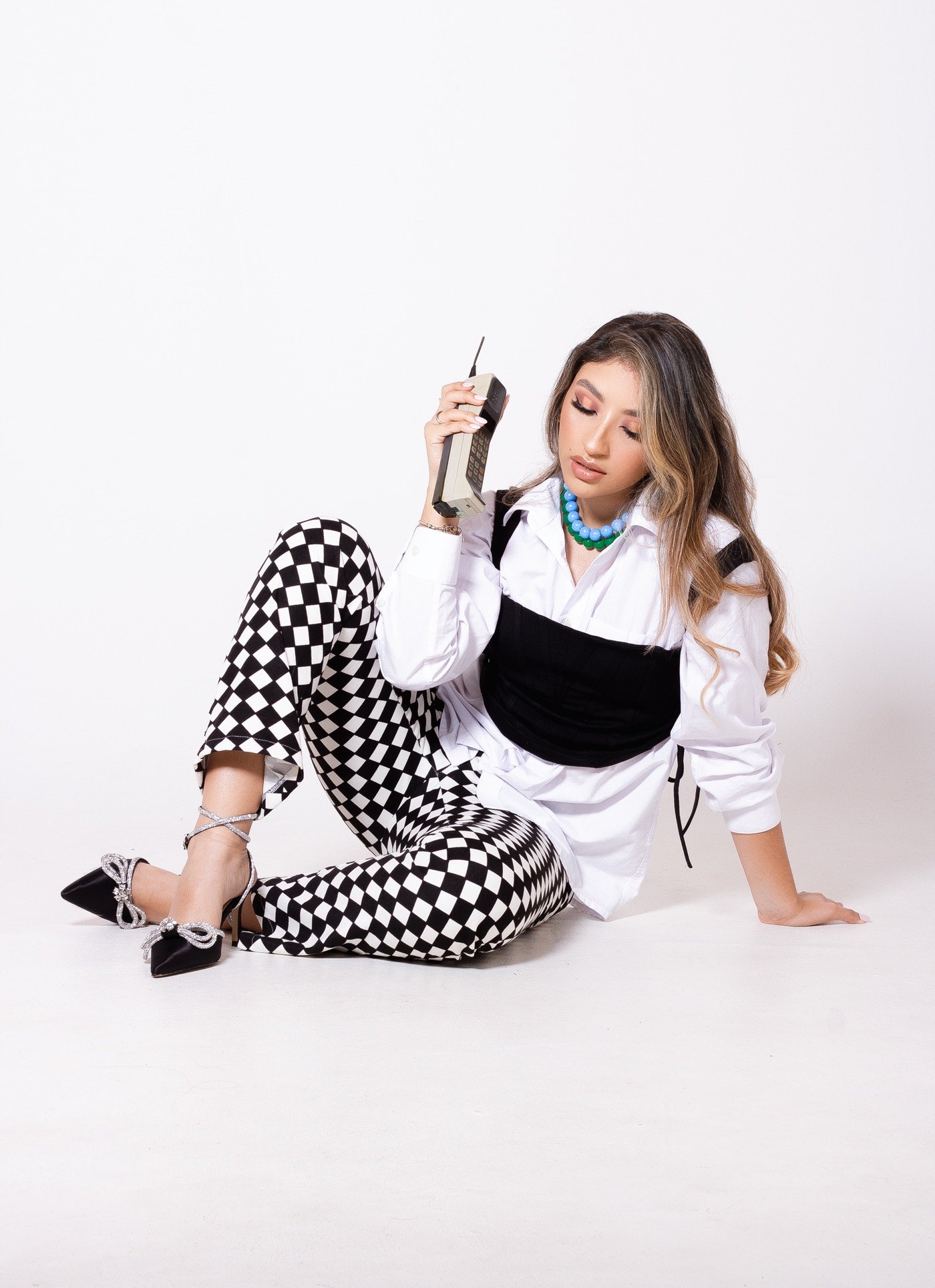Allison López sentada con pantalones de cuadros, camisa blanca y teléfono, fotografía original